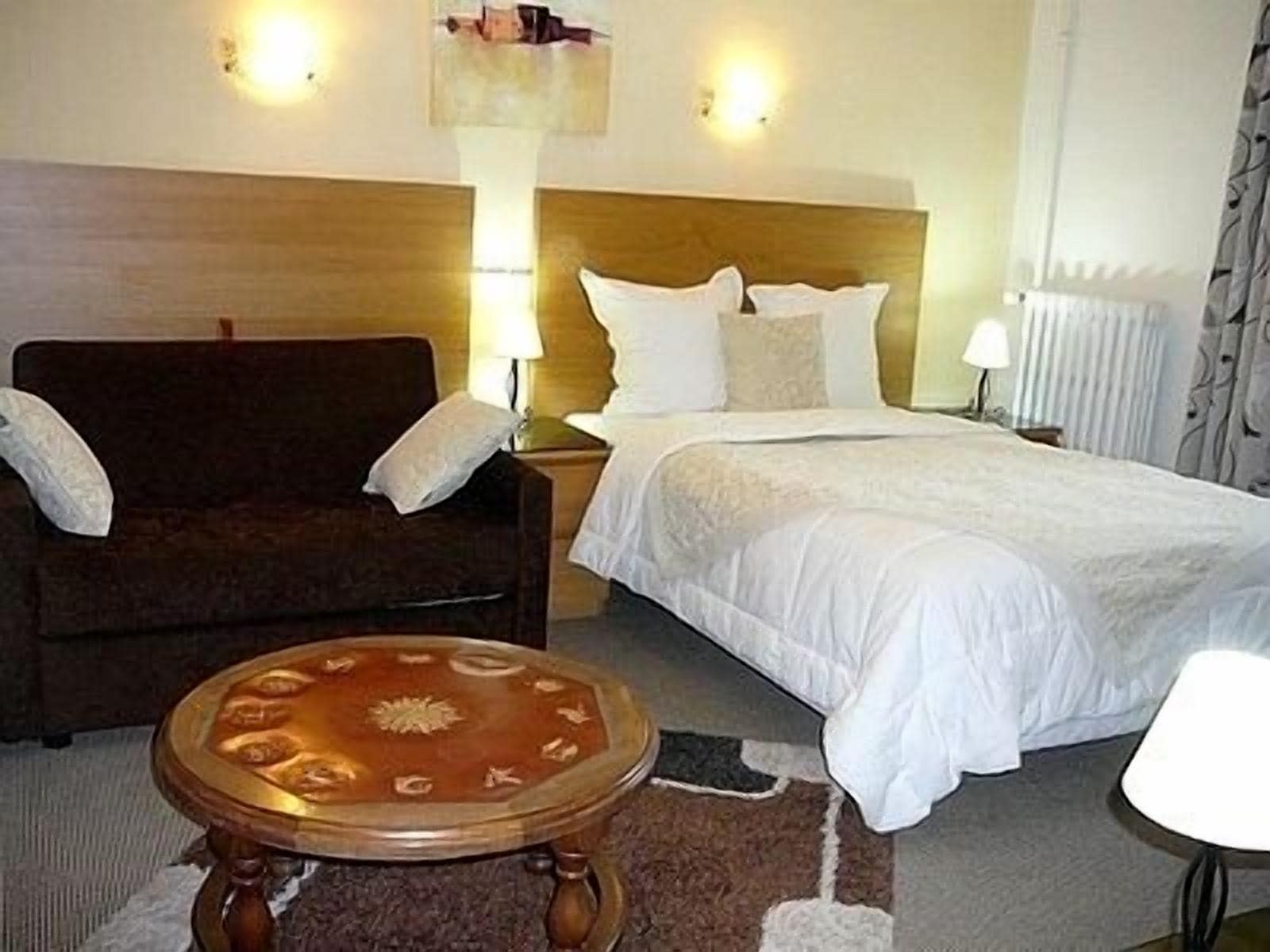 Een hotelkamer met een bed, een houten fauteuil, een kleine ronde tafel en twee bedlampjes.