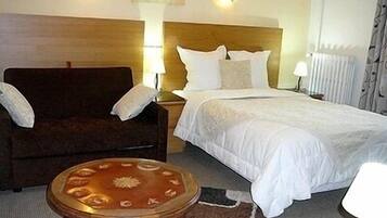 Een hotelkamer met een bed, een houten fauteuil, een kleine ronde tafel en twee bedlampjes.