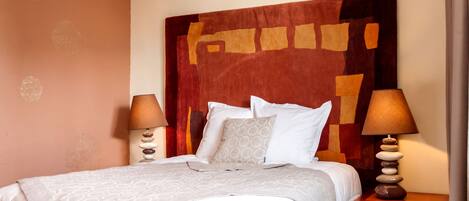 A neatly made bed with a patterned bedspread, two bedside lamps, and a wooden nightstand with a stack of stones.