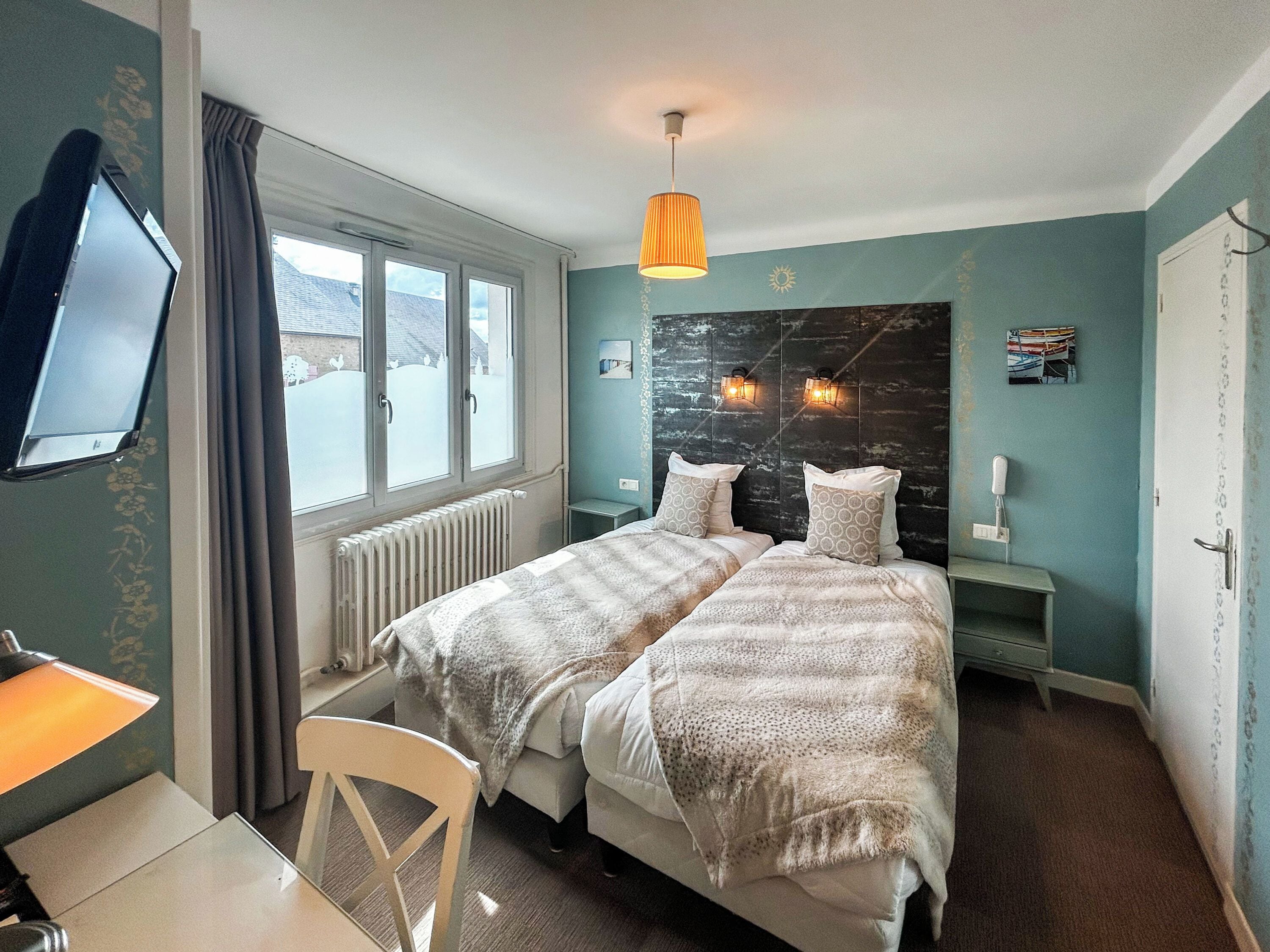 Une chambre avec deux lits, un bureau, une chaise, une télévision et une fenêtre avec des rideaux.