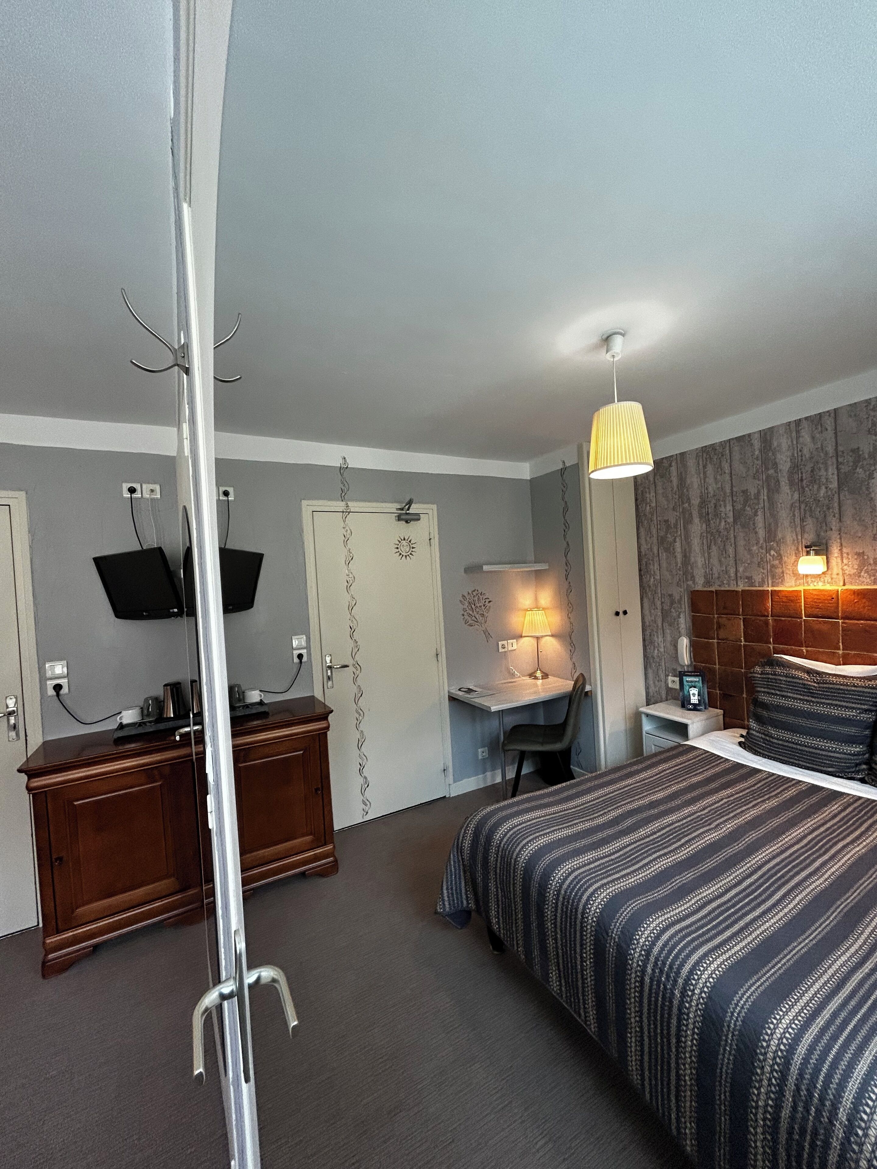 A hotel room with a bed, desk, chair, and a mirror.