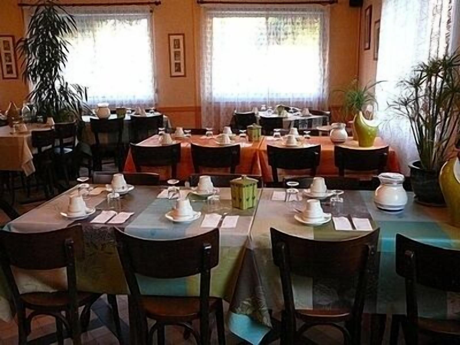 A restaurant with multiple tables set for dining, chairs, and potted plants.