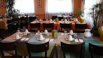 Un restaurante con varias mesas dispuestas para comer, sillas y plantas en macetas.