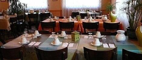 A restaurant with multiple tables set for dining, chairs, and potted plants.