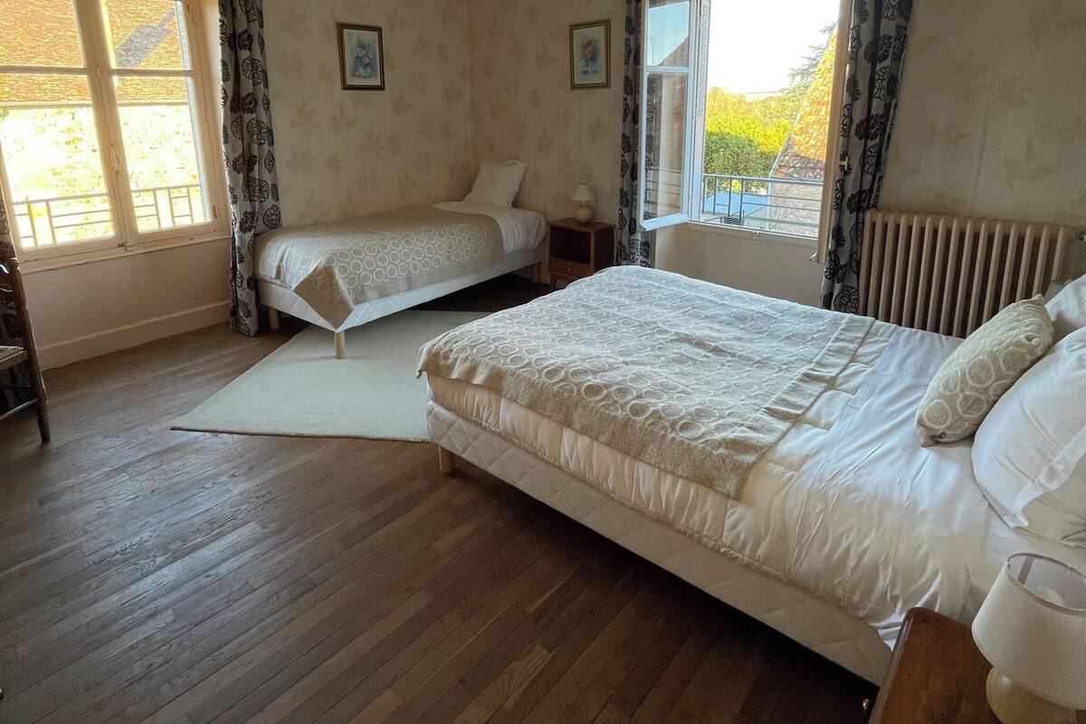 A bedroom with two beds, a wooden floor, and a window with curtains.