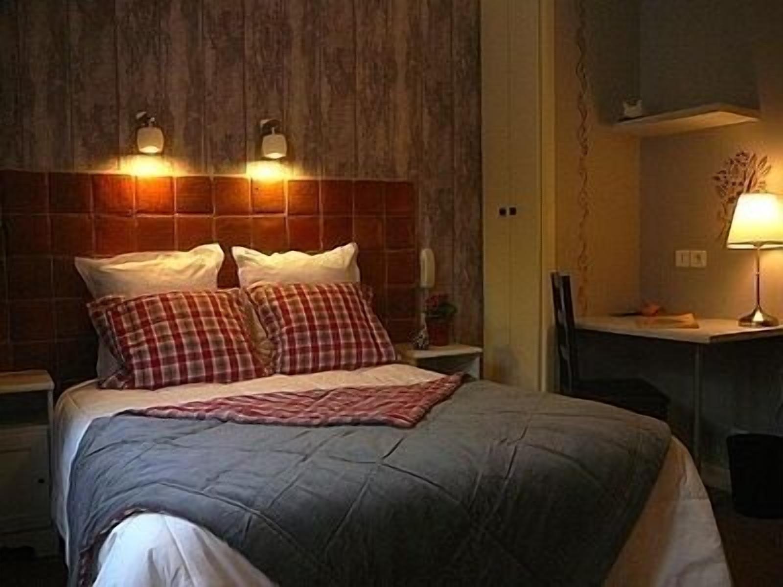 A hotel room with a bed, two bedside lamps, a desk with a chair, and a wall-mounted telephone.