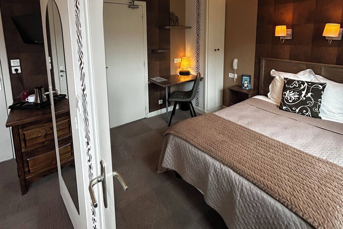 A hotel room with a bed, desk, chair, and a mirror.