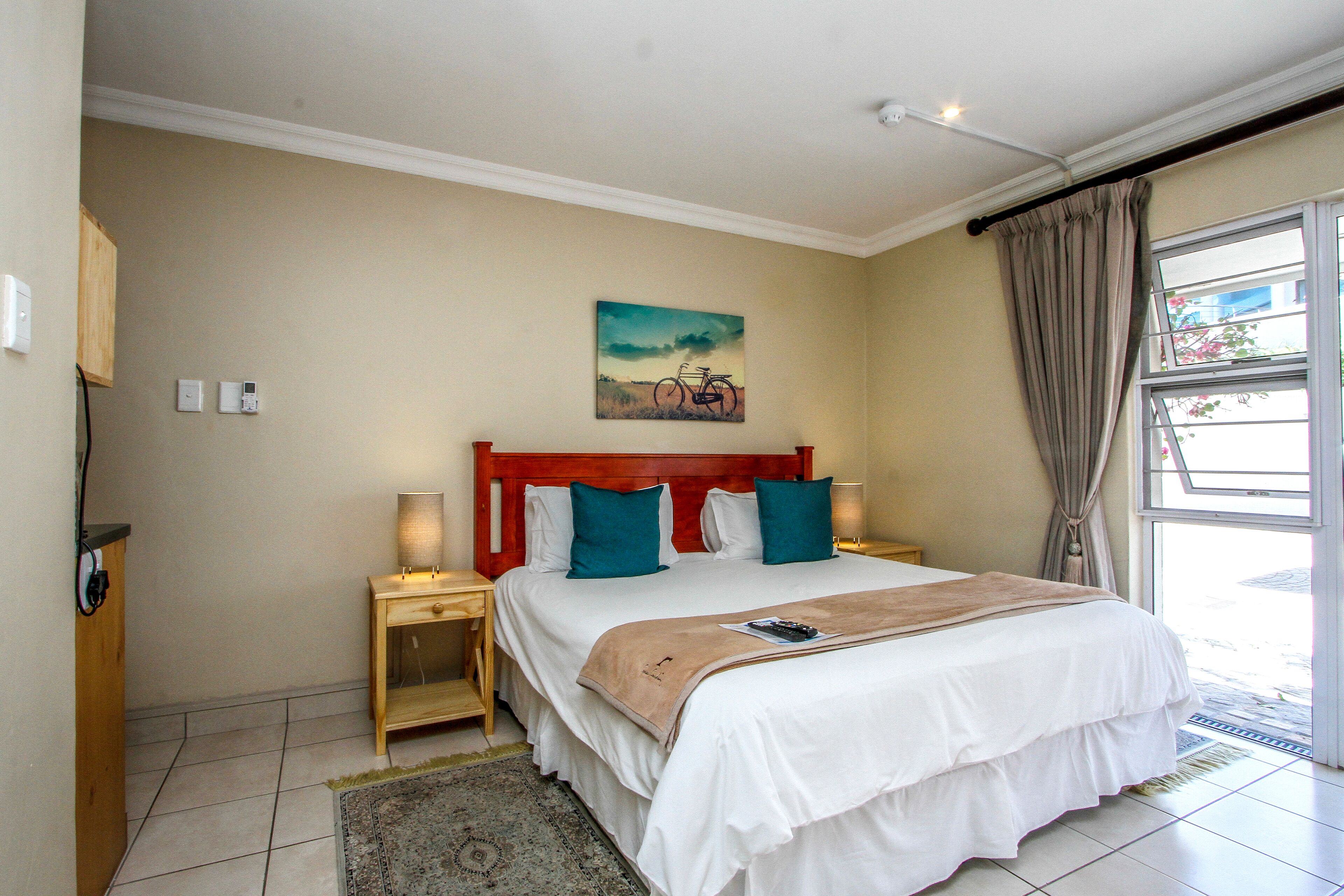 A bedroom with a large bed, a nightstand, a lamp, a painting, and a window with curtains.