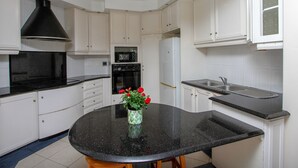 A kitchen with white cabinets, a black countertop, a black stove, and a white refrigerator. - THE SANDRINGHAM B&B AND SELF-CATERING (Umhlanga)