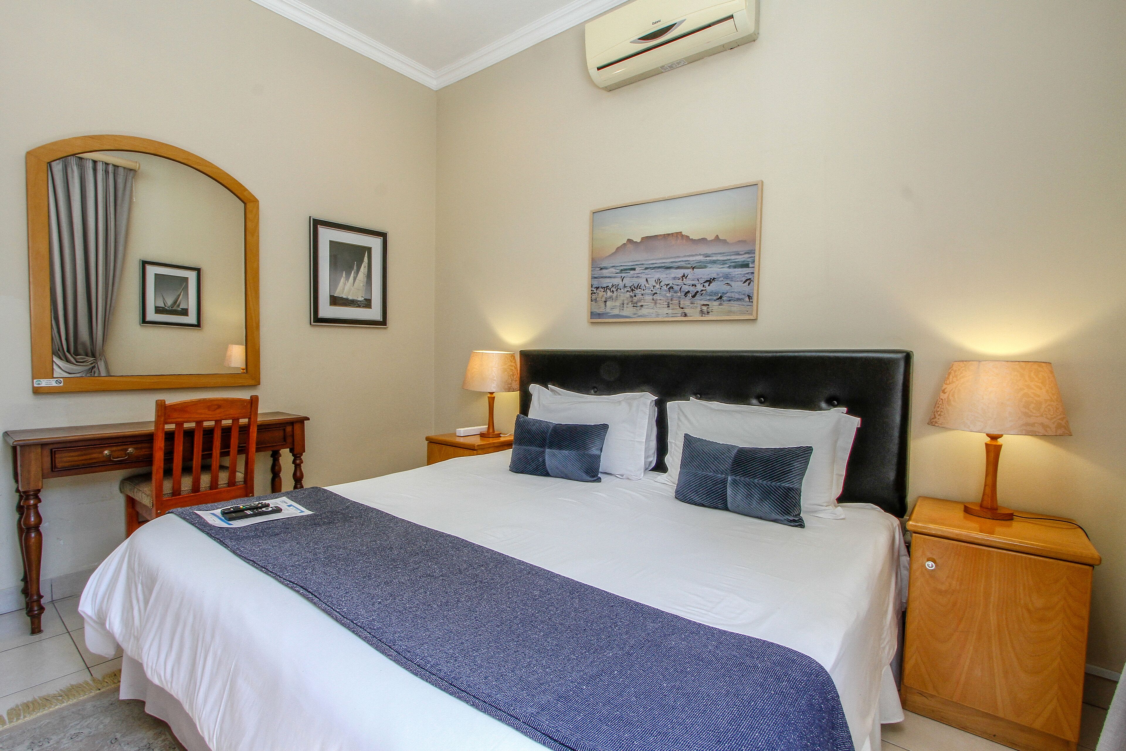 A hotel room with a large bed, two bedside tables with lamps, a desk, a chair, and a large mirror.