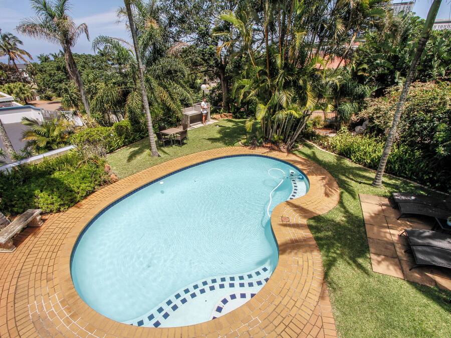 A swimming pool surrounded by a brick deck, with a patio area and outdoor furniture.