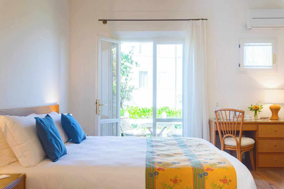 Habitación de hotel con cama, escritorio, silla, ventana y equipo de aire acondicionado.