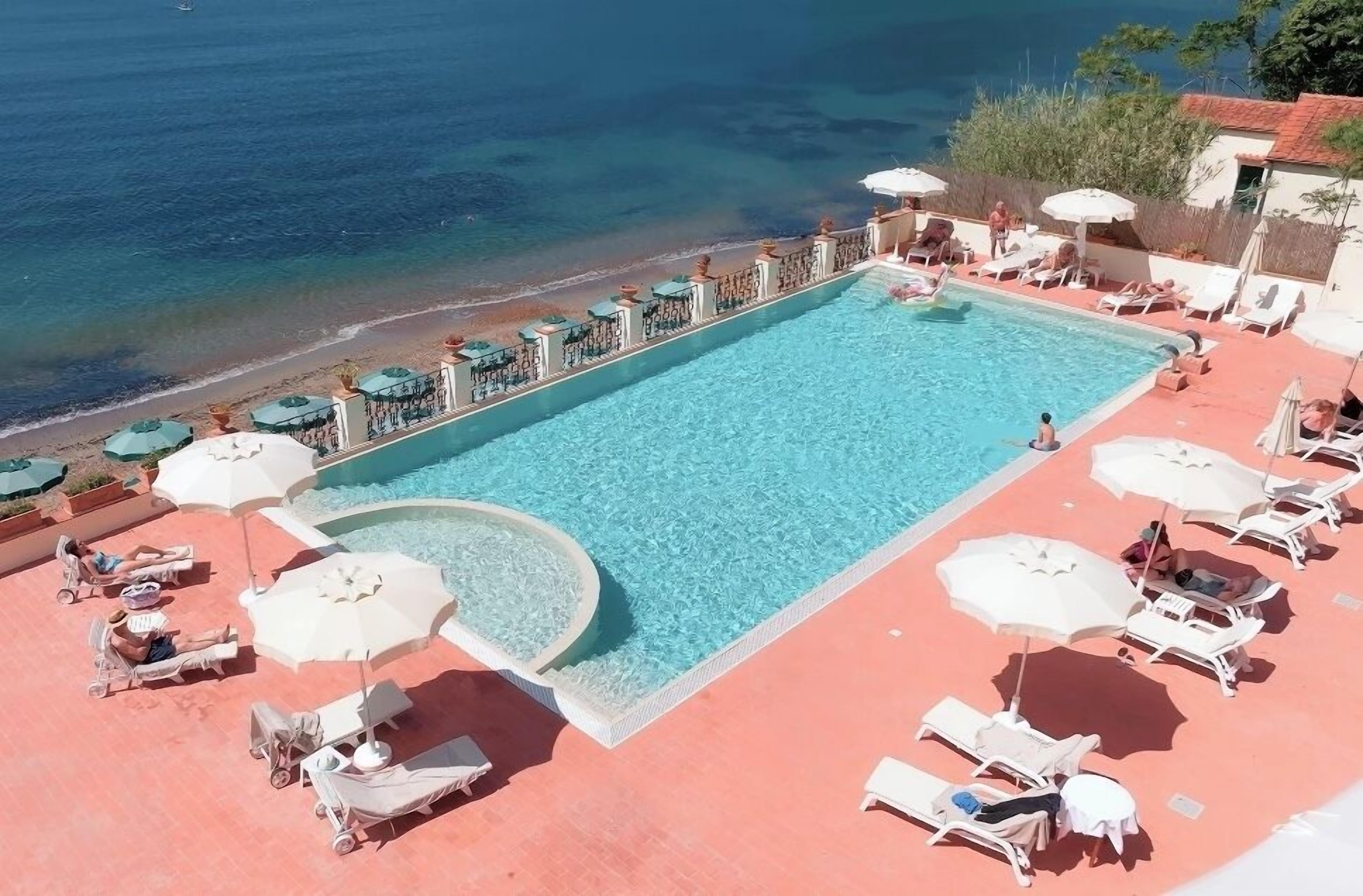 A pool with lounge chairs and umbrellas, a beach view, and a clear sky.