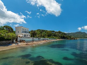 Un hotel frente al mar con playa, aguas cristalinas y montañas al fondo.