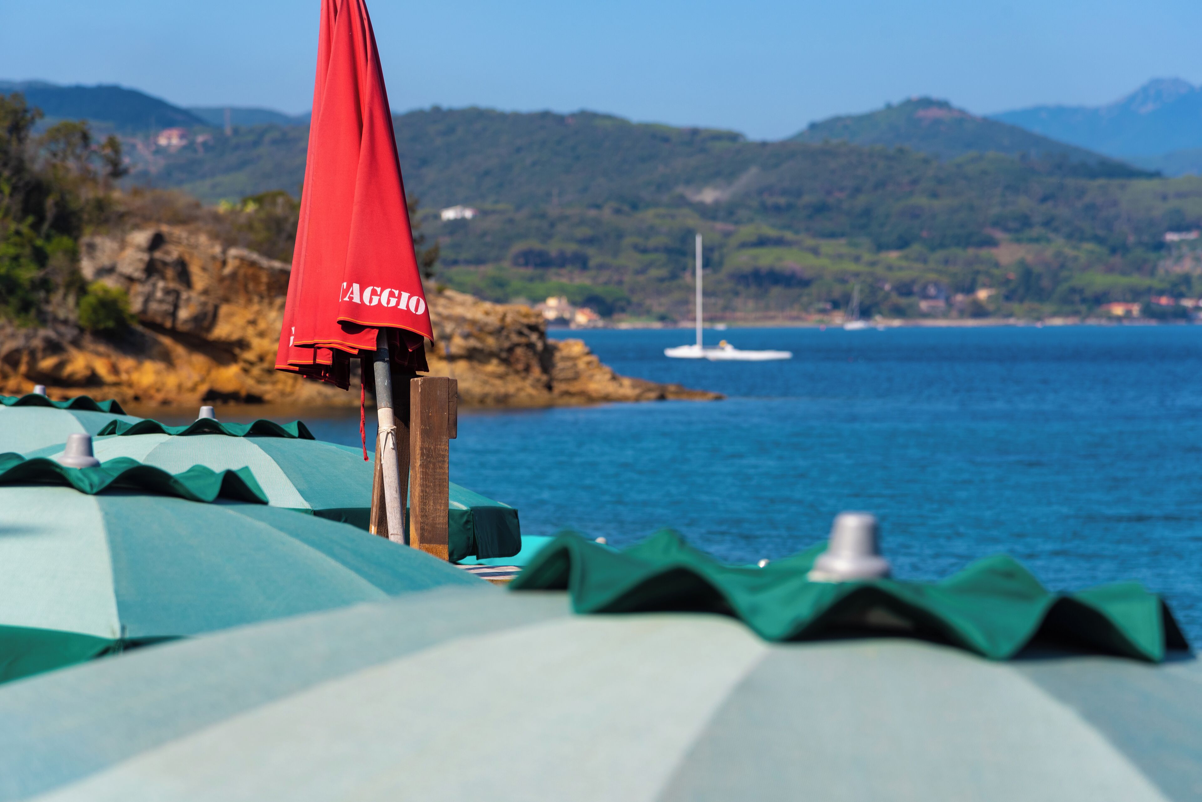 A beachside view with umbrellas and a sailboat in the distance.