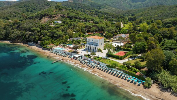 Eine Luftaufnahme eines Küstenresorts mit Strand, Villen und einem Tennisplatz.