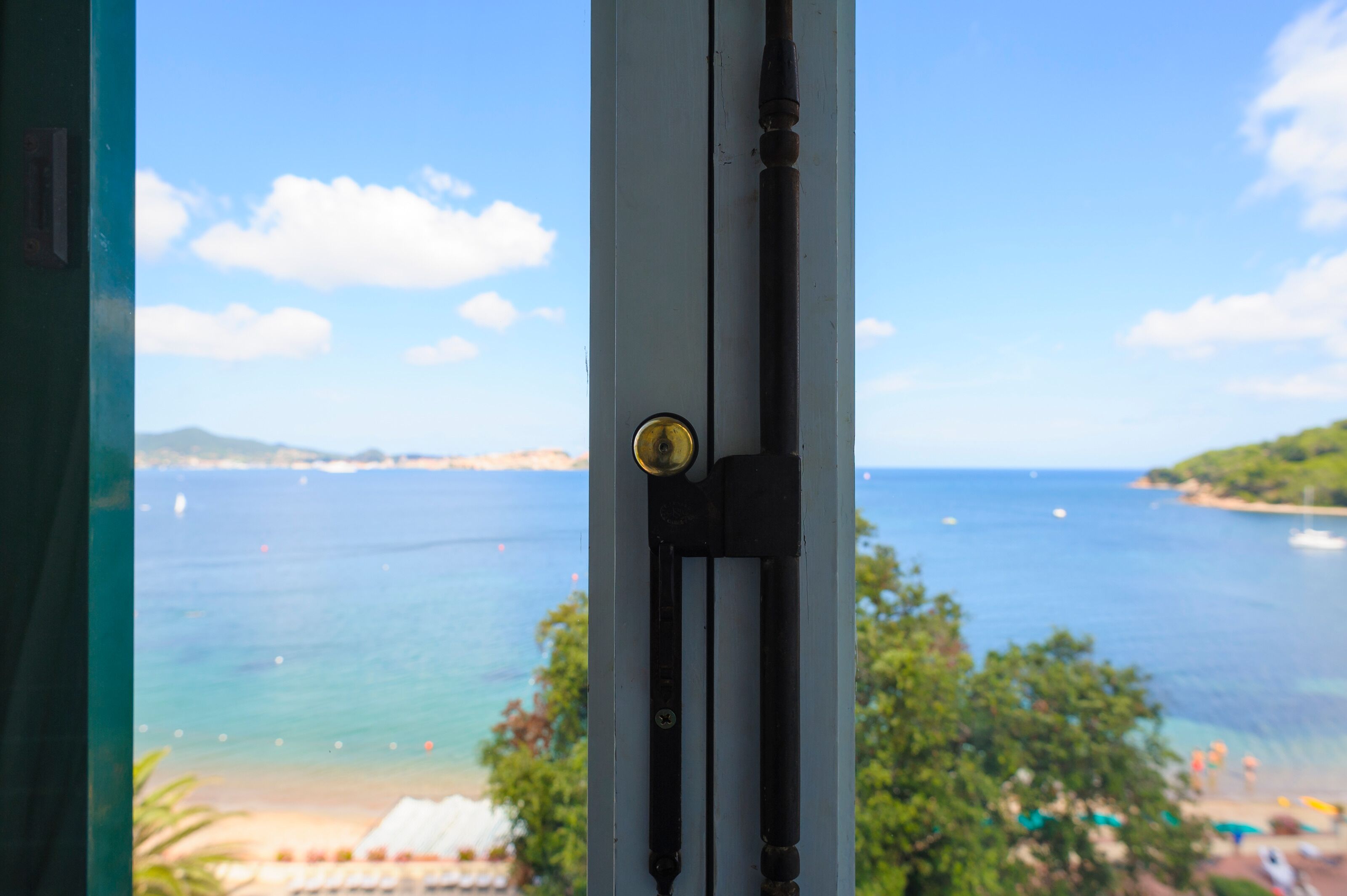 Vista de una zona costera a través de una ventana, con un picaporte y un candado a la vista.