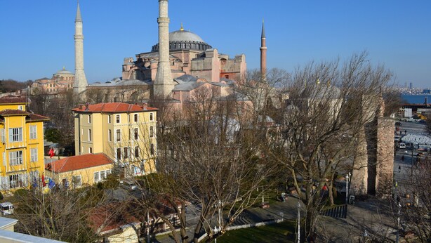 A historic building with multiple minarets and domes, surrounded by modern buildings and a park. - Ares Hotel Sultanahmet (Istanbul)