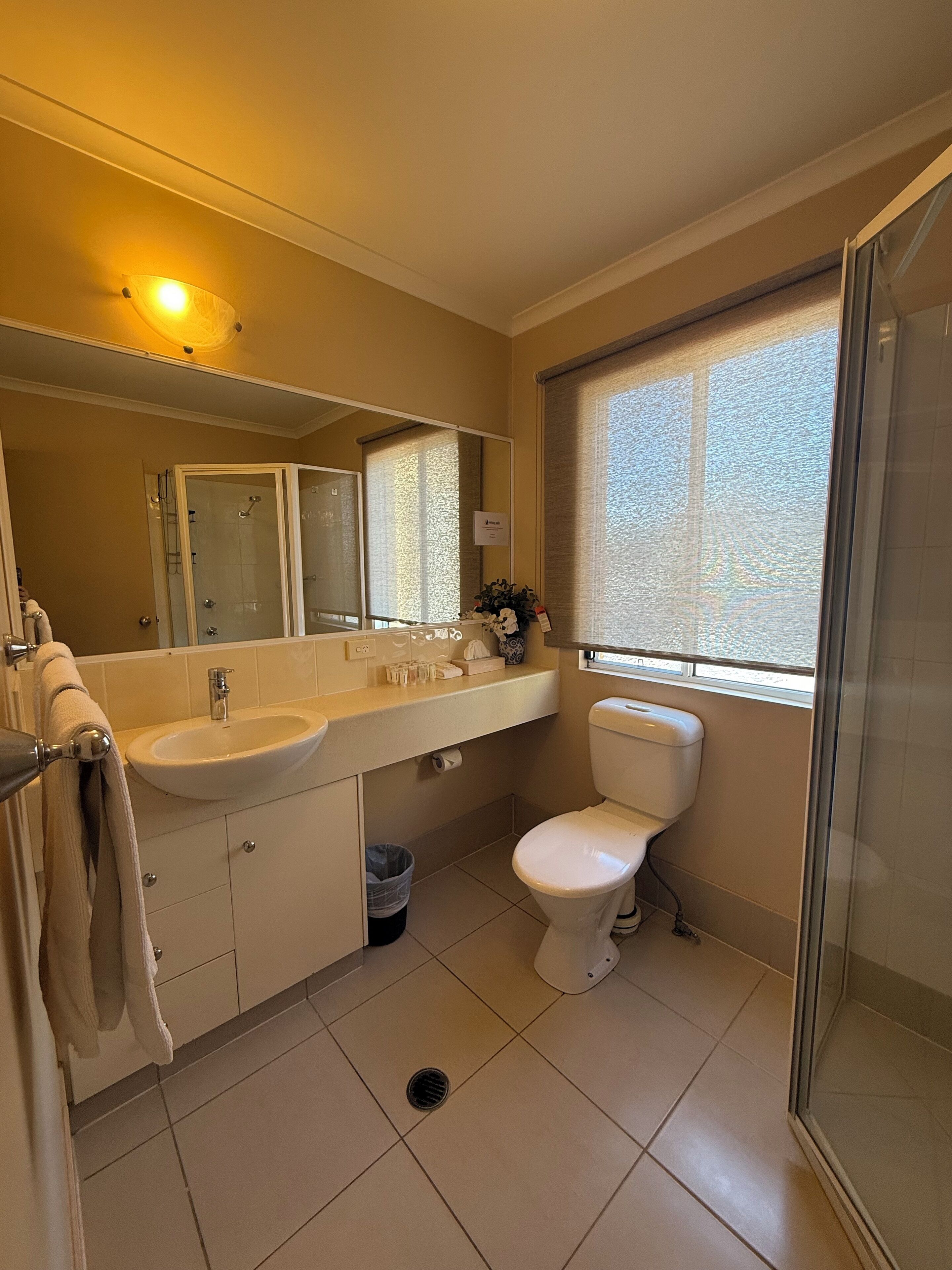 Un baño con dos lavamanos, un inodoro, una ducha y una ventana con persianas.