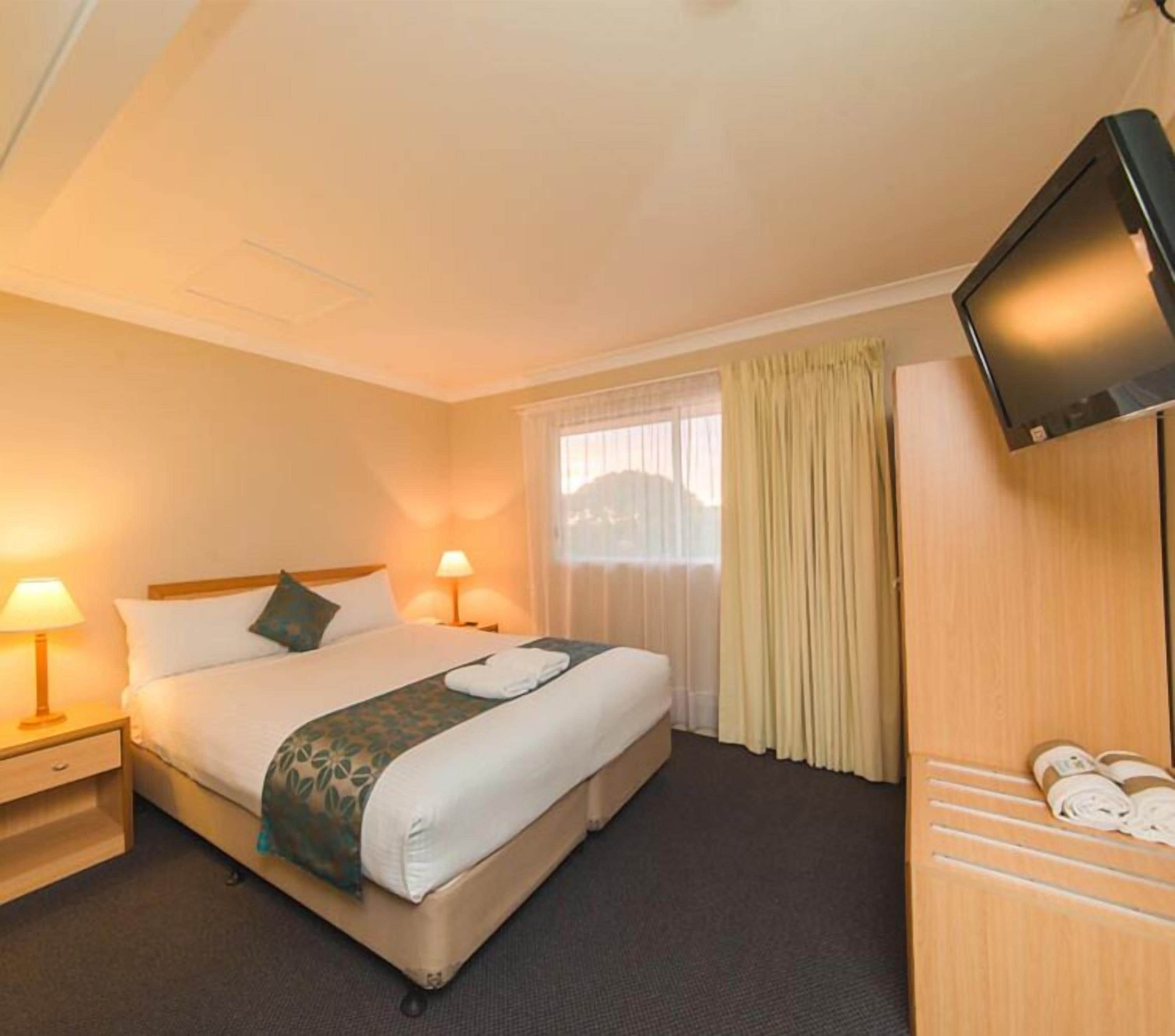 A hotel room with a bed, two bedside lamps, a TV, and a window with curtains.