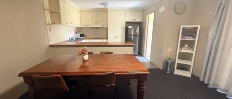 Un espacio habitable compacto con una mesa de comedor y sillas, una kitchenette, un refrigerador pequeño y una estantería empotrada.
