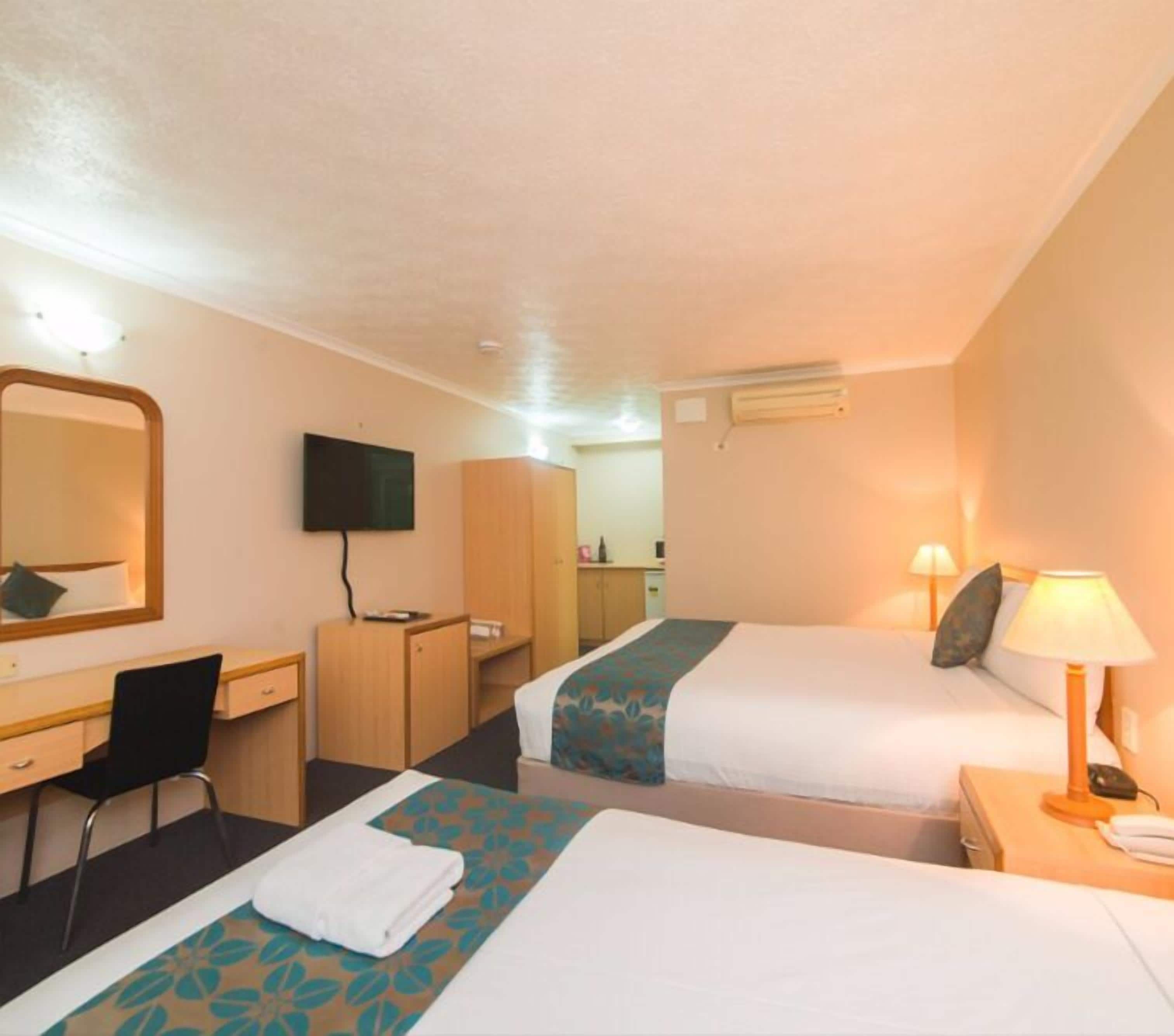 A hotel room with two beds, a desk, a chair, a TV, and a wardrobe.