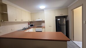 A compact kitchen with a central island, a microwave, a stove, and a refrigerator. - Harbour Sails Motor Inn (Gladstone)