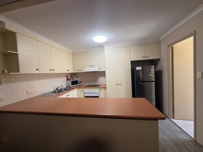A compact kitchen with a central island, a microwave, a stove, and a refrigerator. - Harbour Sails Motor Inn (Gladstone)