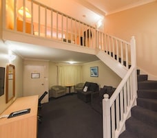 A hotel room with a staircase leading to an upper level, a seating area with sofas and a small table, and a desk with a computer.