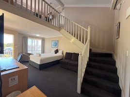 Una habitación de hotel con cama, sofá, escritorio y una escalera.