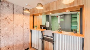 A reception desk with a wooden finish, a mirror above it, and a potted plant on the counter. - B&B HOTEL Mulhouse Sausheim (Sausheim)