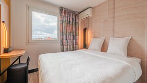 A hotel room with a large bed, a desk with a chair, and a window with curtains. - B&B HOTEL Mulhouse Sausheim (Sausheim)