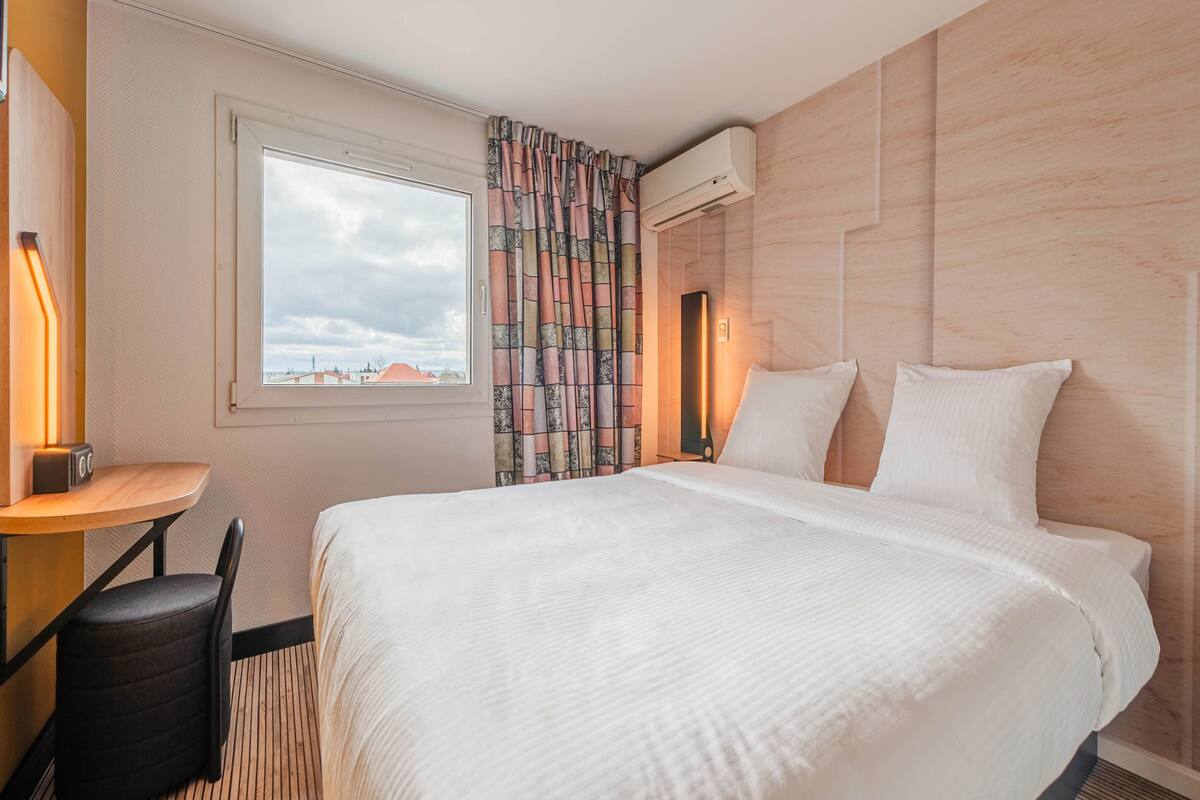 A hotel room with a large bed, a desk with a chair, and a window with curtains.