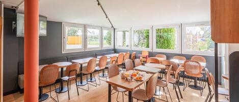 Un comedor moderno con varias mesas y sillas, ventanas amplias y un techo con conductos a la vista.