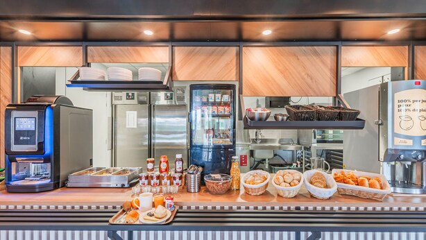 A breakfast bar with a coffee machine, a refrigerator, and various food items. - B&B HOTEL Mulhouse Sausheim (Sausheim)