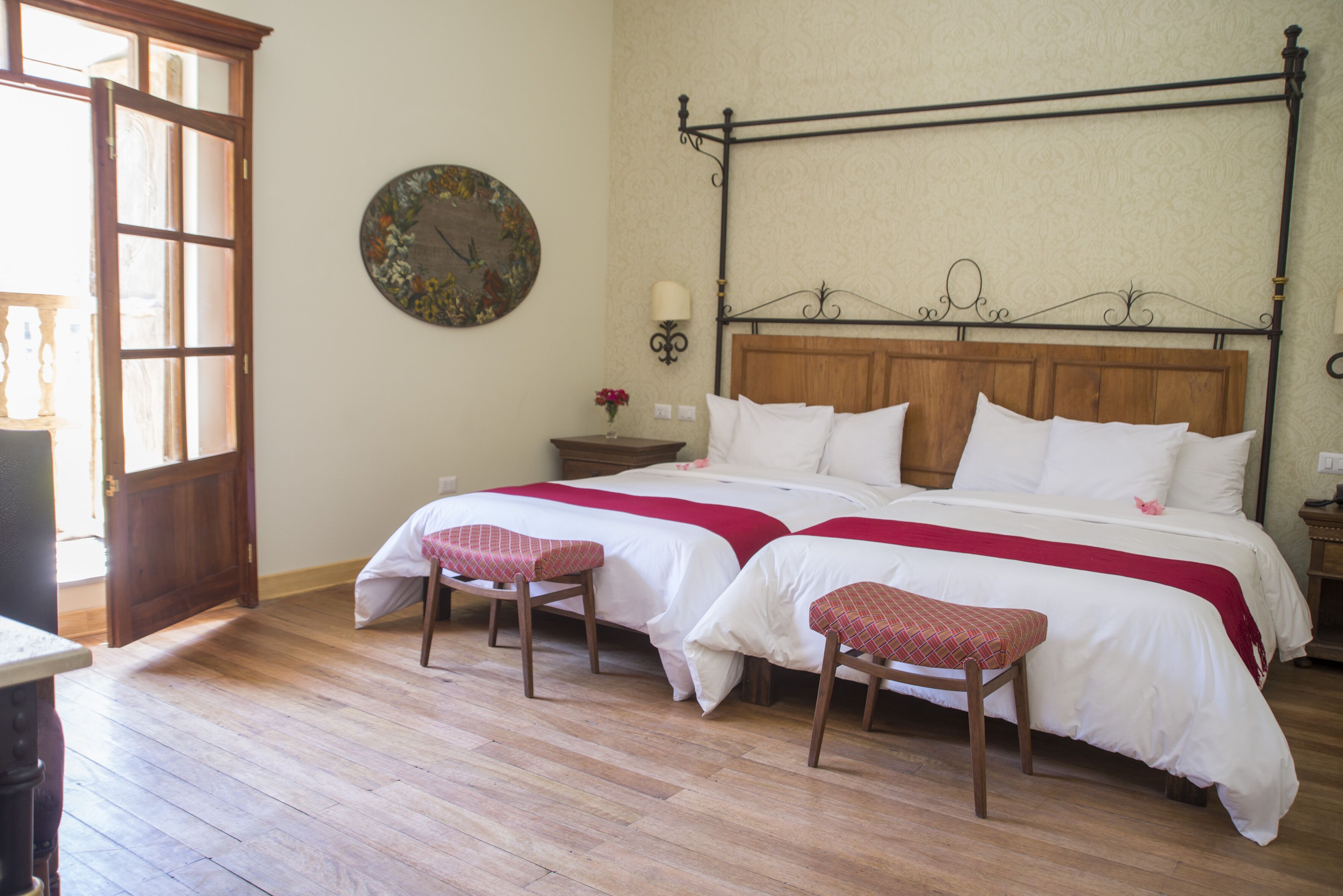 A bedroom with a four-poster bed, two bedside tables, a round wall clock, and a wooden floor.