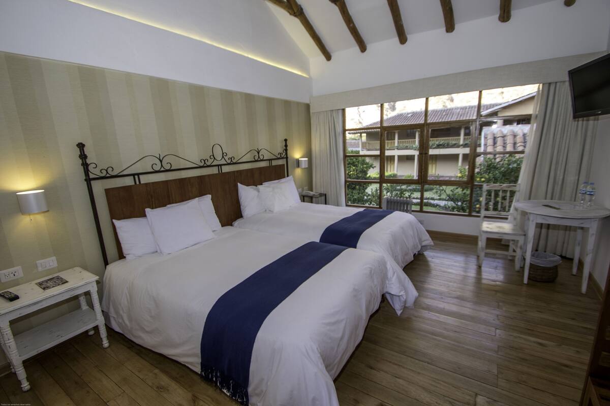 Une chambre d’hôtel avec deux lits, une petite table, un téléviseur et une fenêtre donnant sur des immeubles.