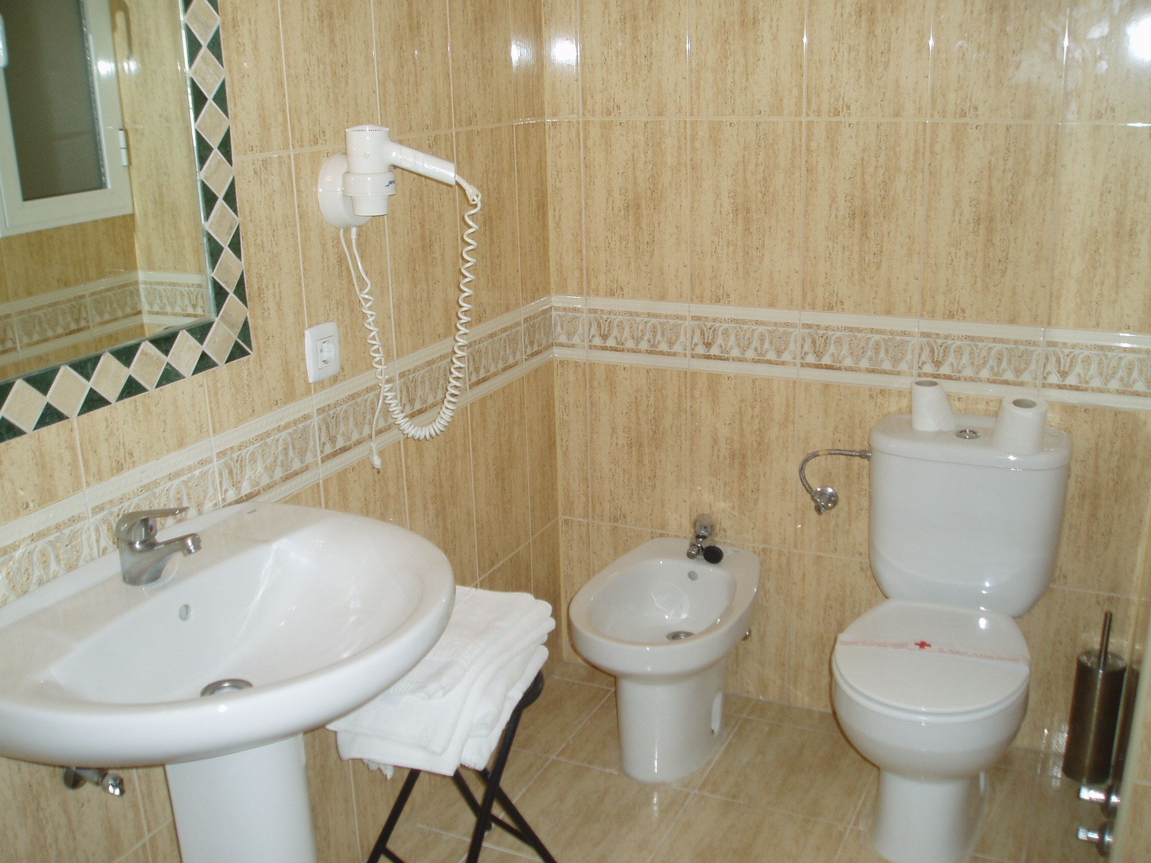 A bathroom with a sink, bidet, toilet, and a hairdryer mounted on the wall.