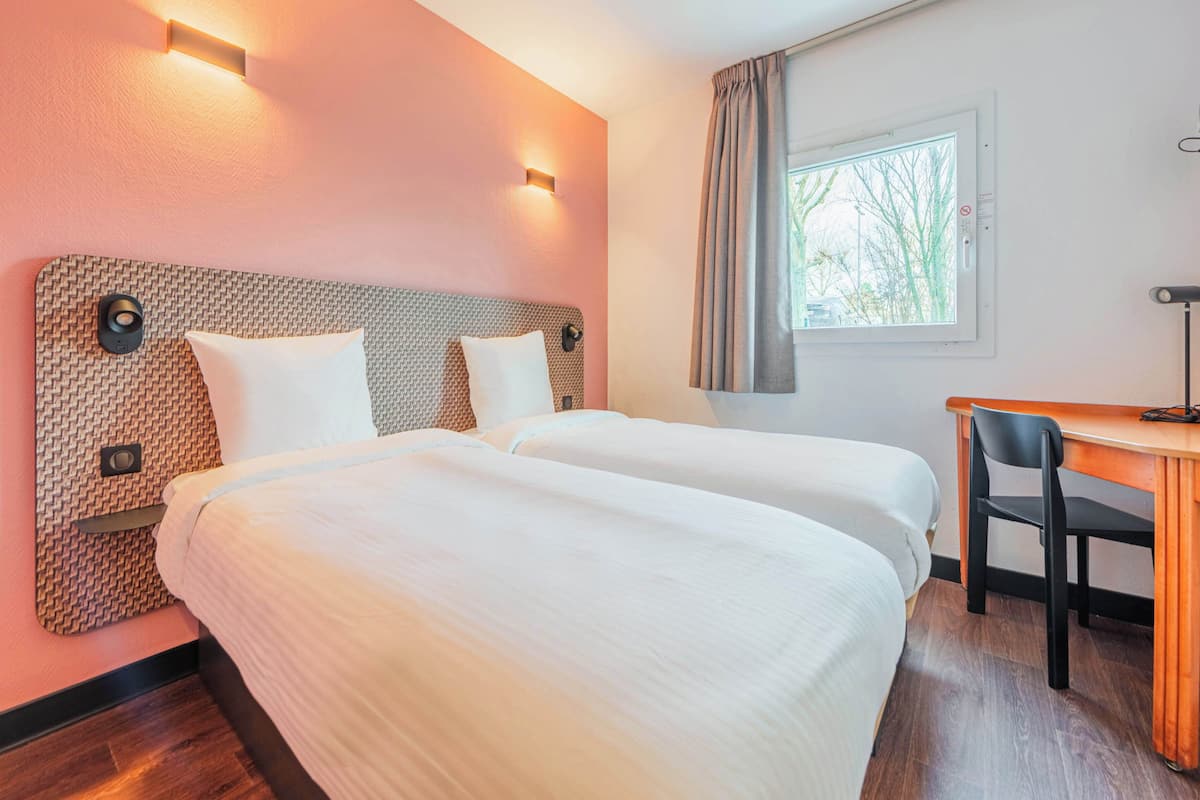 A hotel room with two beds, a desk, and a chair.