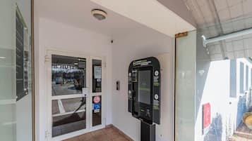 Entrada de un hotel con puerta de cristal, un quiosco de seguridad y suelo de baldosas.
