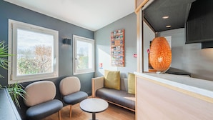 A modern room with a sofa, two chairs, a small table, and a kitchen area with a unique orange light fixture. - B&B HOTEL Strasbourg Nord Mundolsheim (Mundolsheim)
