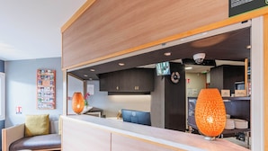 A modern reception area with a wooden counter, seating, and a visible kitchen area in the background. - B&B HOTEL Strasbourg Nord Mundolsheim (Mundolsheim)