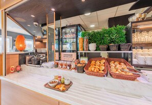A breakfast buffet with various food items, a coffee machine, and a sign in French.