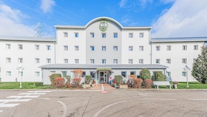 A large, white hotel with a central entrance, multiple windows, and a well-maintained garden area with benches and shrubs. - B&B HOTEL Strasbourg Nord Mundolsheim (Mundolsheim)