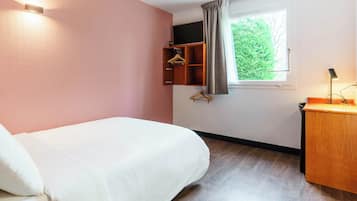 Hotelkamer met een bed, een houten bureau, een kapstok, een raam met uitzicht op groen en een aan de muur bevestigde televisie.