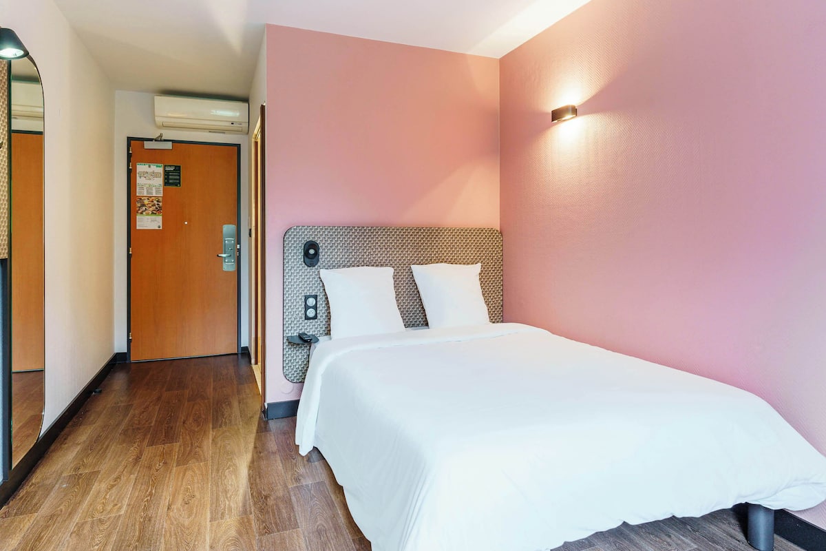 Une chambre d’hôtel avec un plancher en bois, un lit doté d’une tête de lit à motifs et un mur rose.