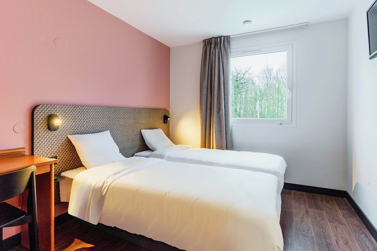 Une chambre d’hôtel avec deux lits, un bureau et une fenêtre donnant sur des arbres.