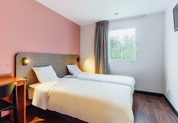 Habitación de hotel con dos camas, un escritorio y ventana con vistas a árboles.