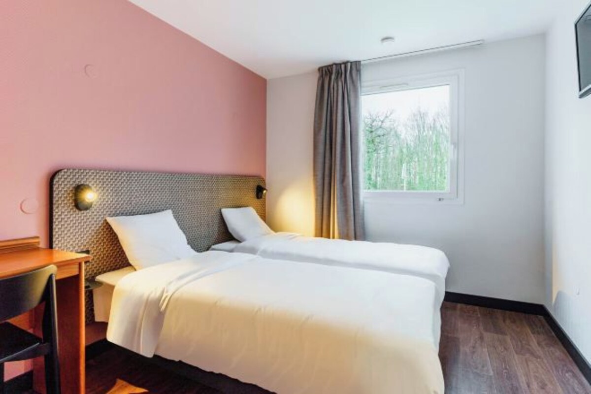 A hotel room with a double bed, a desk, and a window with curtains.
