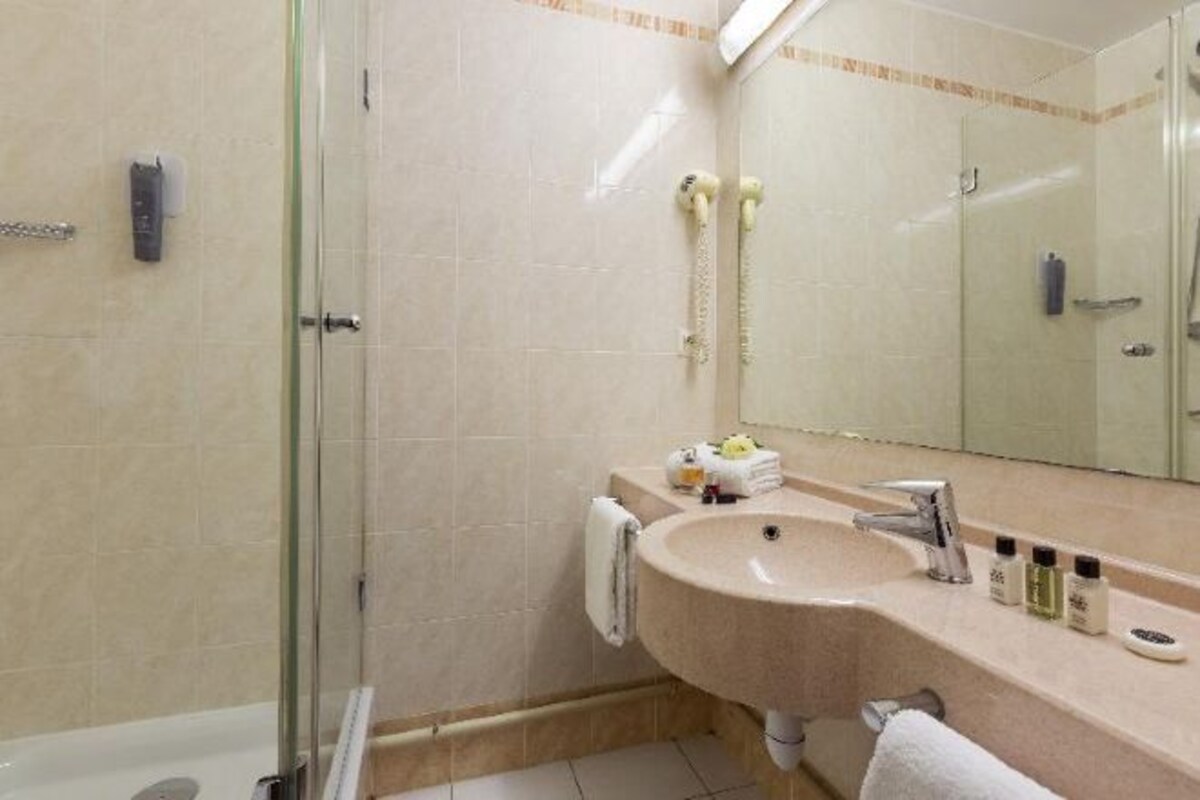 A bathroom with a glass shower enclosure, a sink with a mirror, and toiletries on the counter.